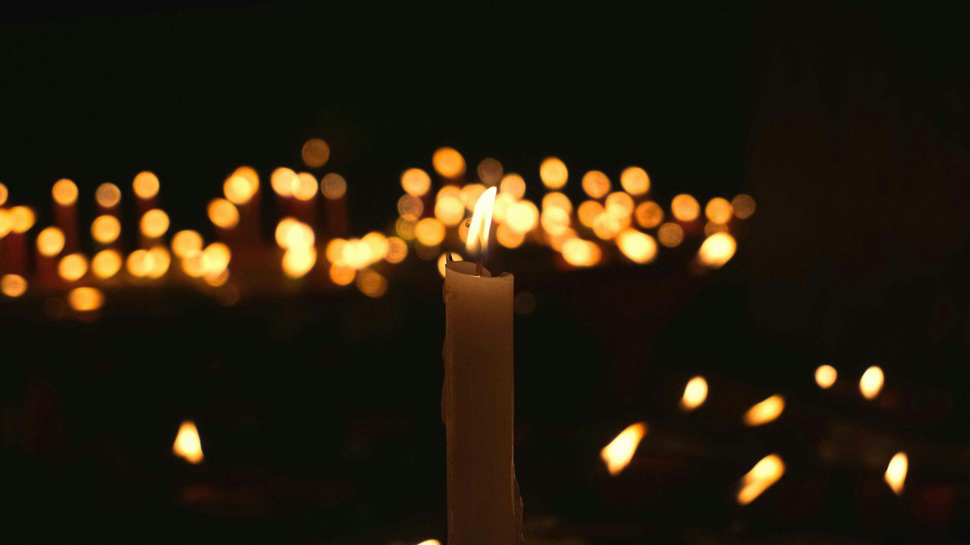 Set against a dark background, a candle flickers in the foreground, surrounded by other candles.
