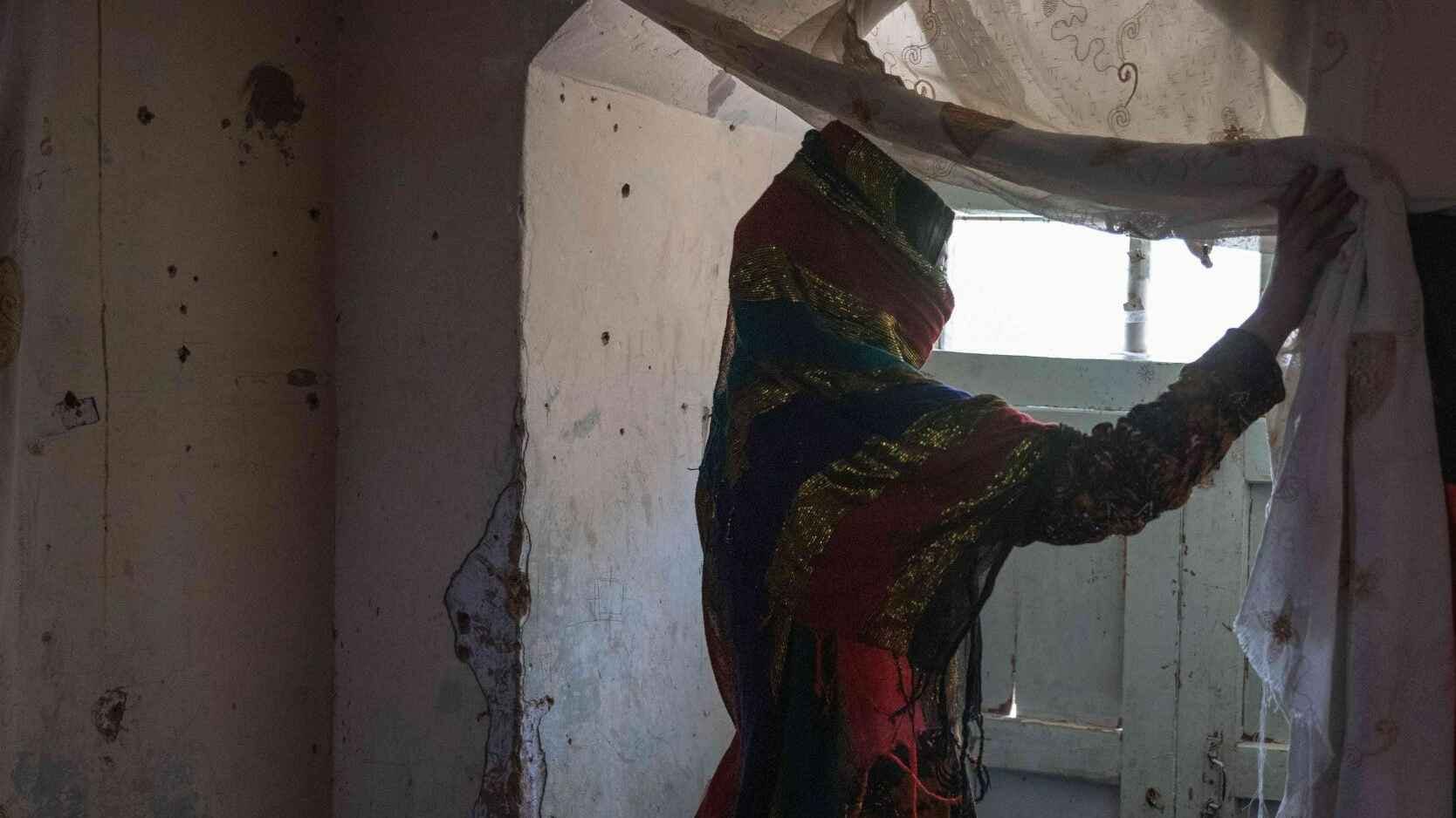 A veiled Afghan woman peers whistfully out the slit above her door.