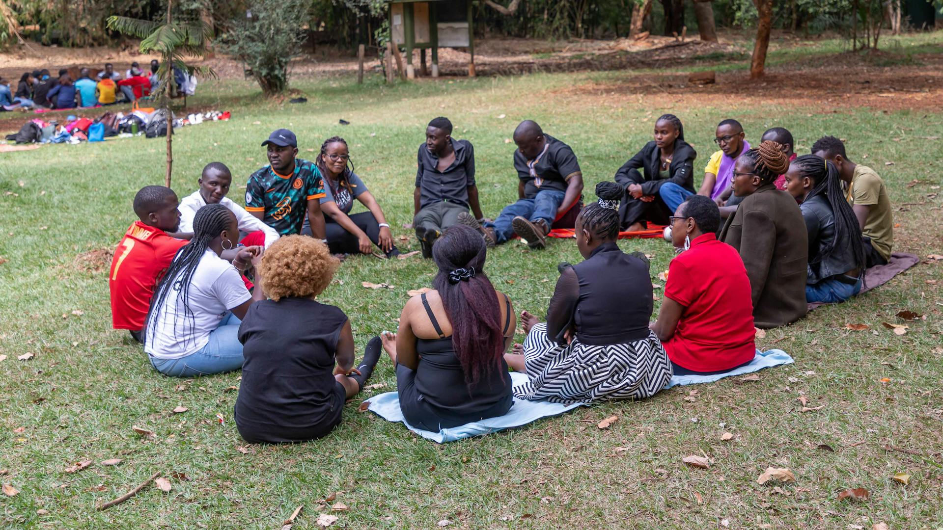 A group of youth having a group therapy session, seated on the grass in a circle..