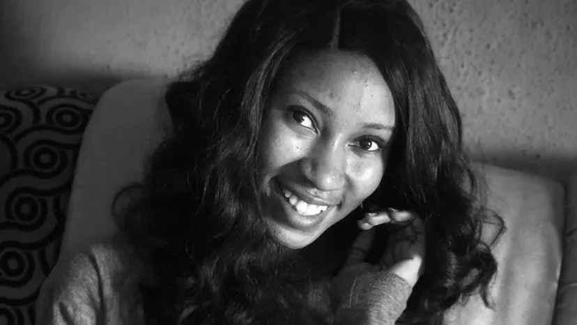 Anita Nwokoji smiles at the camera with her hand framing her face. The image is close up and black and white. Anita had dark long hair and dark eyes. She's wearing a long-sleeved shirt.