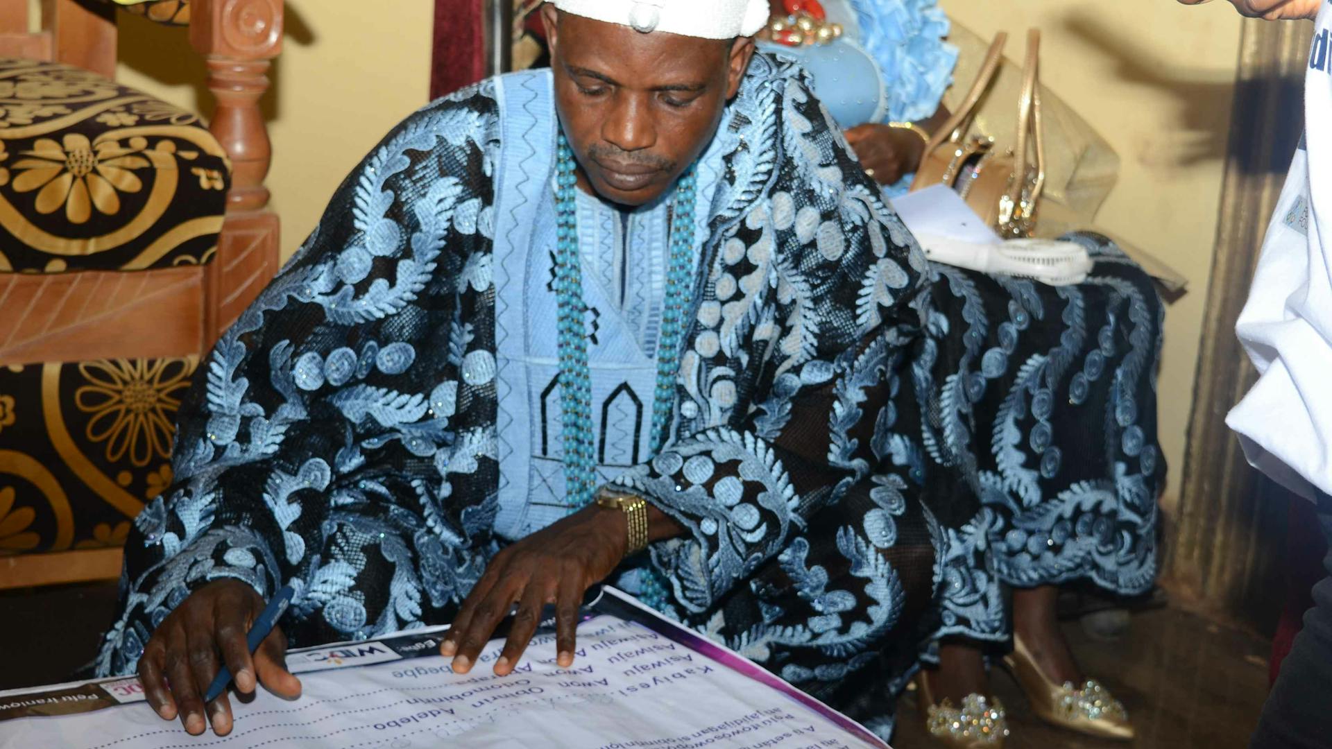 Image shows a male Nigerian leader signing an oath to decry domestic violence. 