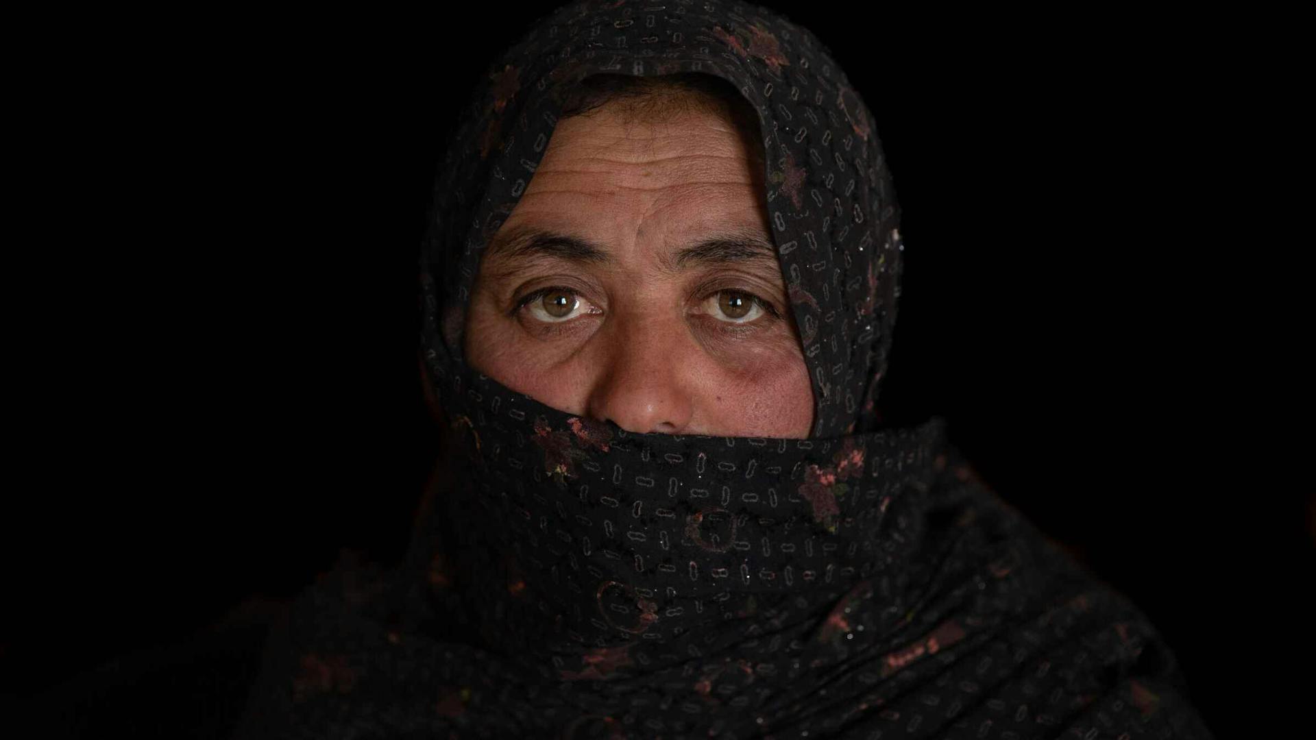 A woman in a black hijab stares at the camera, against a black background