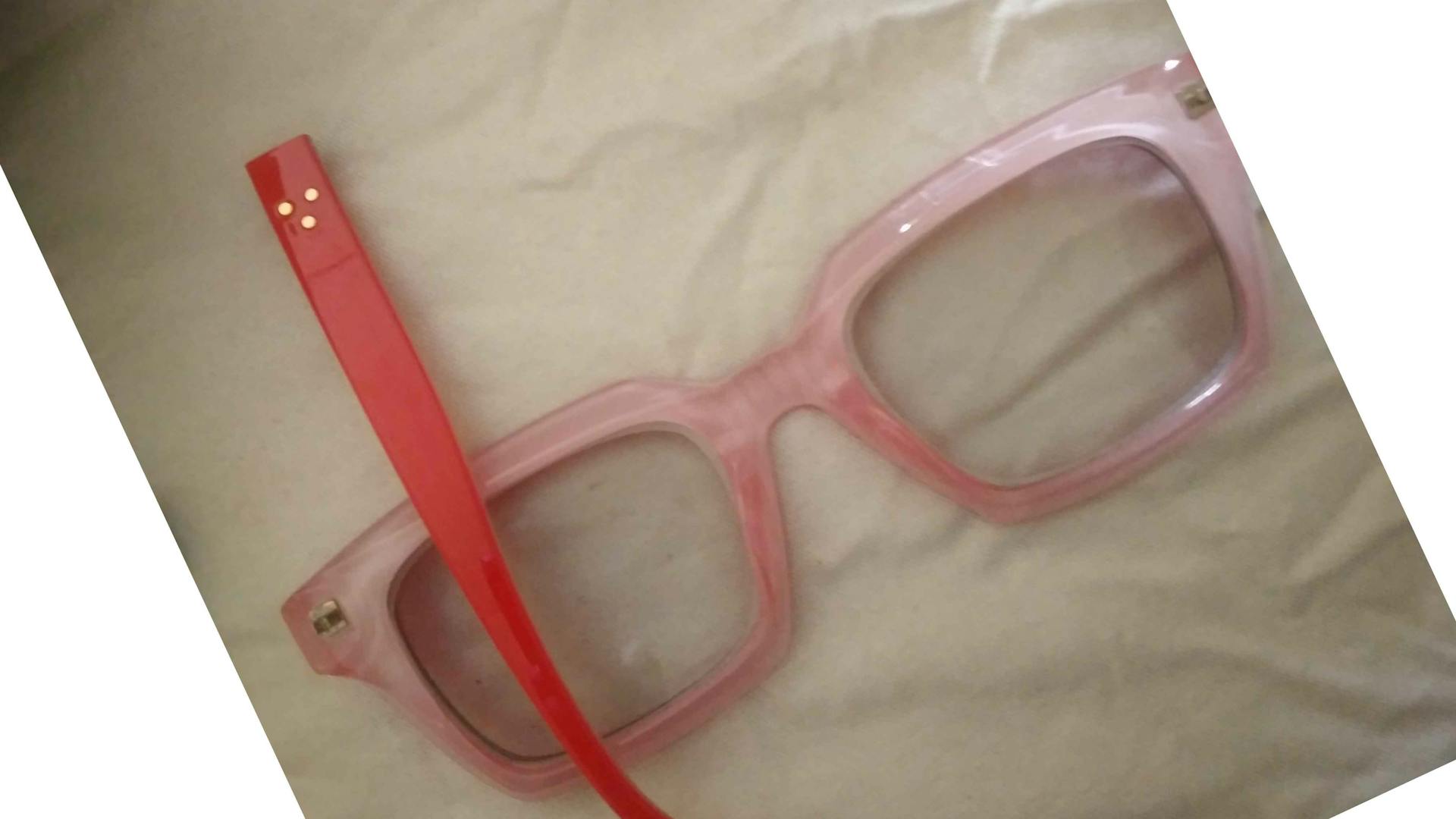 Red square framed glasses, lying on their lenses, with the handles broken off and one handle resting on the left side.