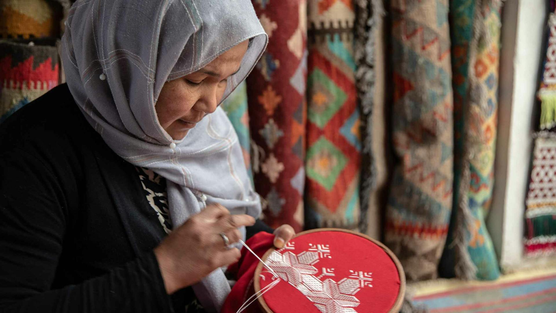 A middle-aged Afghan woman in a headscarf embroiders in her home.
